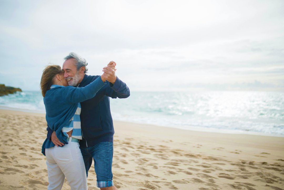 enior couple joyfully dancing together on a sandy beach during sunset